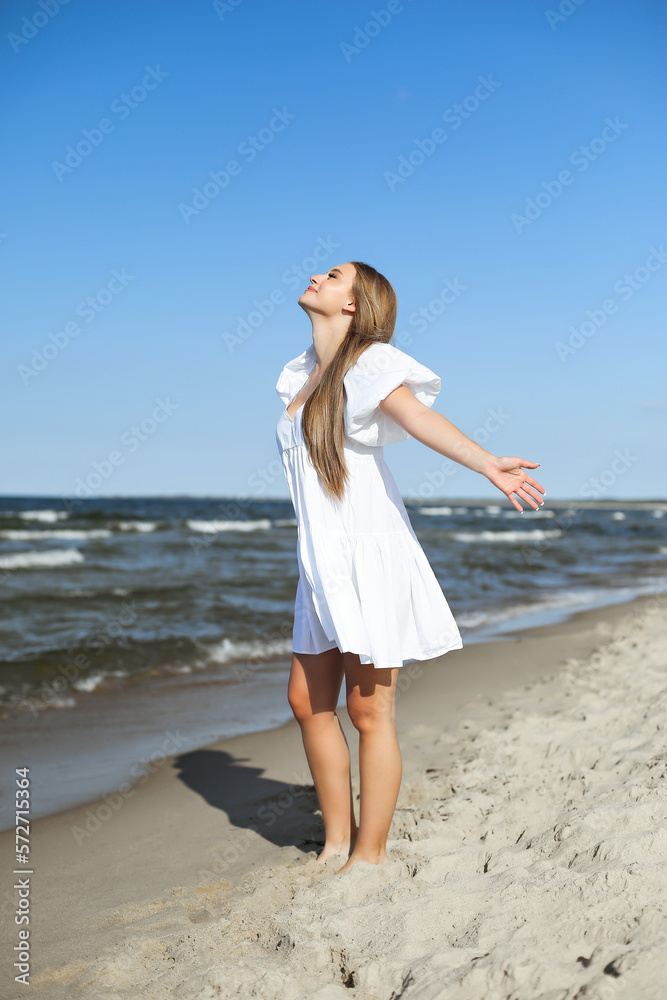 Happy smiling beautiful woman is on the ocean beach in a white summer dress, open arms Happy smiling beautiful woman is on the ocean beach in a white summer dress, open arms