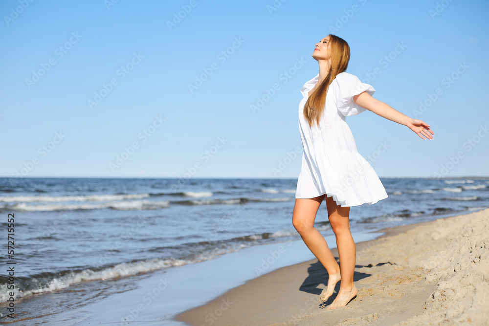 Happy smiling beautiful woman is walking on the ocean beach with open arms Happy smiling beautiful woman is walking on the ocean beach with open arms