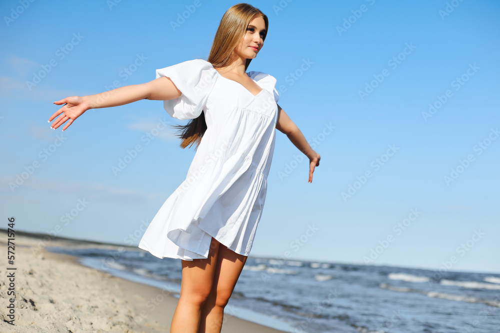Happy, beautiful woman on the ocean beach standing in a white summer dress, open arms Happy, beautiful woman on the ocean beach standing in a white summer dress, open arms