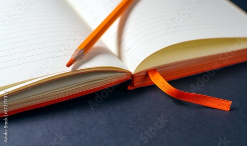 An orange pencil lies on the open page of the diary on a black background. A stylish concept of office supplies for business. Selective focus, copy space.