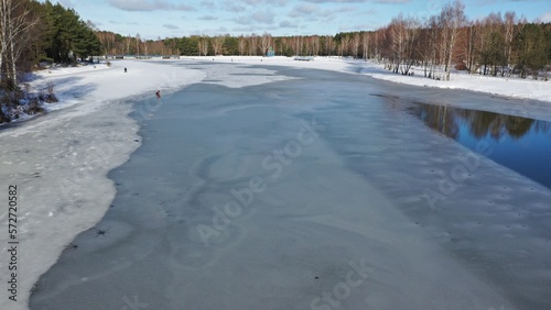 Fototapeta Naklejka Na Ścianę i Meble -  Dangerous spring fishing on melted ice. Ice-covered lake with polynyas. Lake in the forest in the mountains with water partially covered with ice. Fishermen fishing in winter.