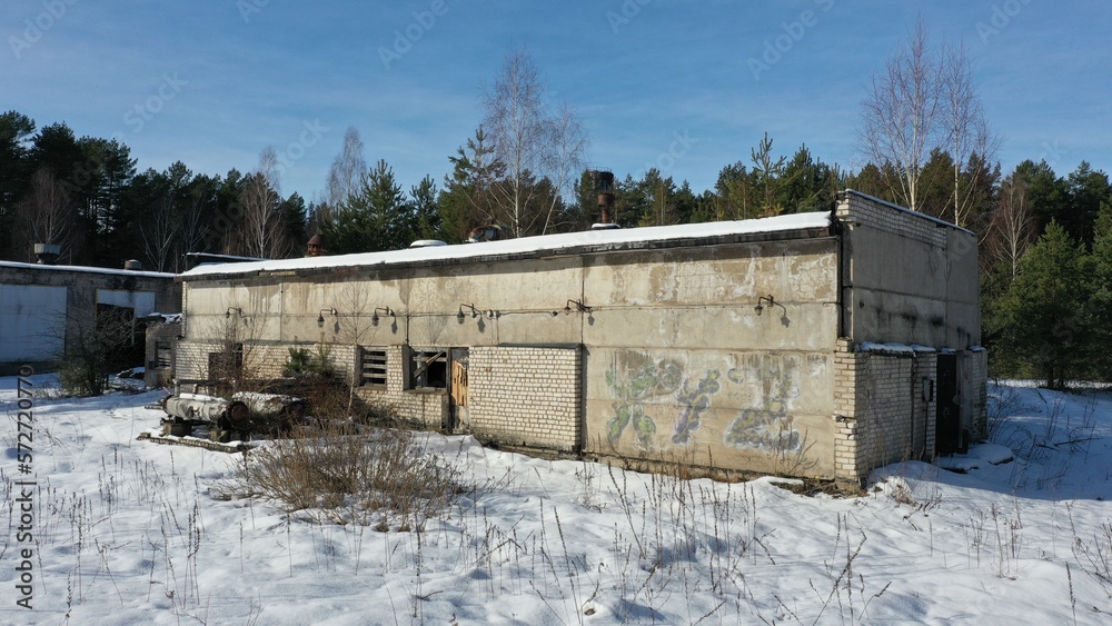The abandoned building of the oil-fired boiler house of the former Soviet recreation center. An old boiler house under a layer of snow in the middle of a pine forest. Ruins in the middle of the forest