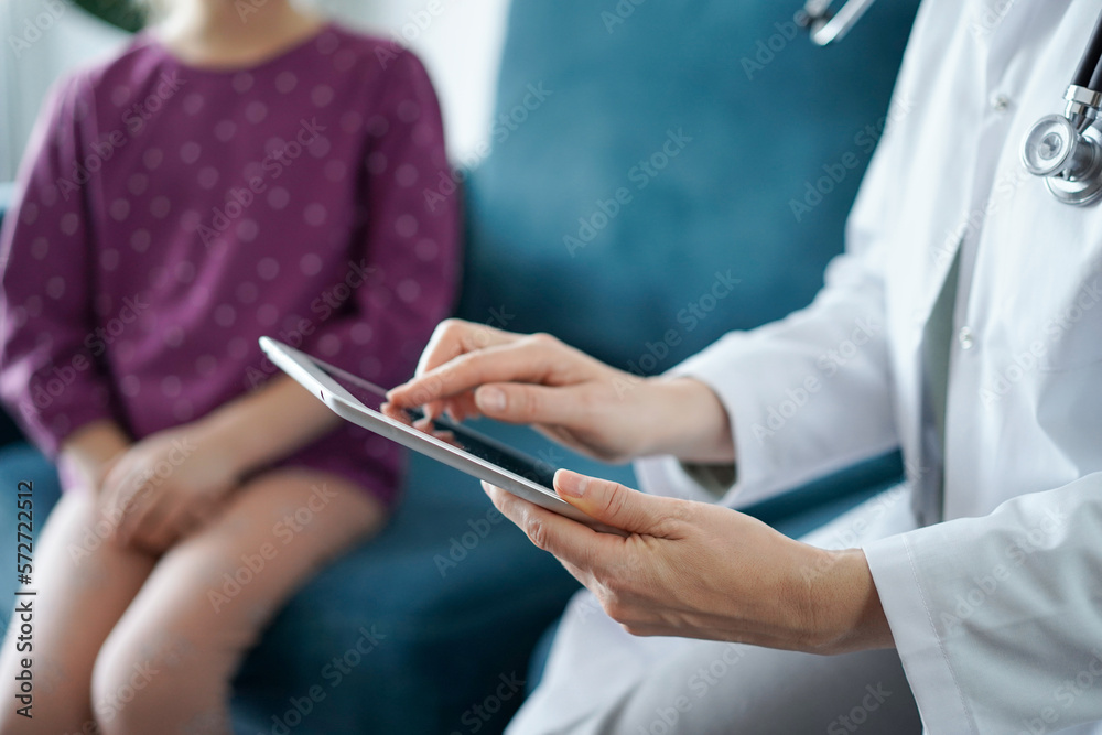 Doctor woman and kid patient at home. The pediatrician uses a tablet computer, close up. Medicine, healthcare concepts Doctor woman and kid patient at home. The pediatrician uses a tablet computer, close up. Medicine, healthcare concepts