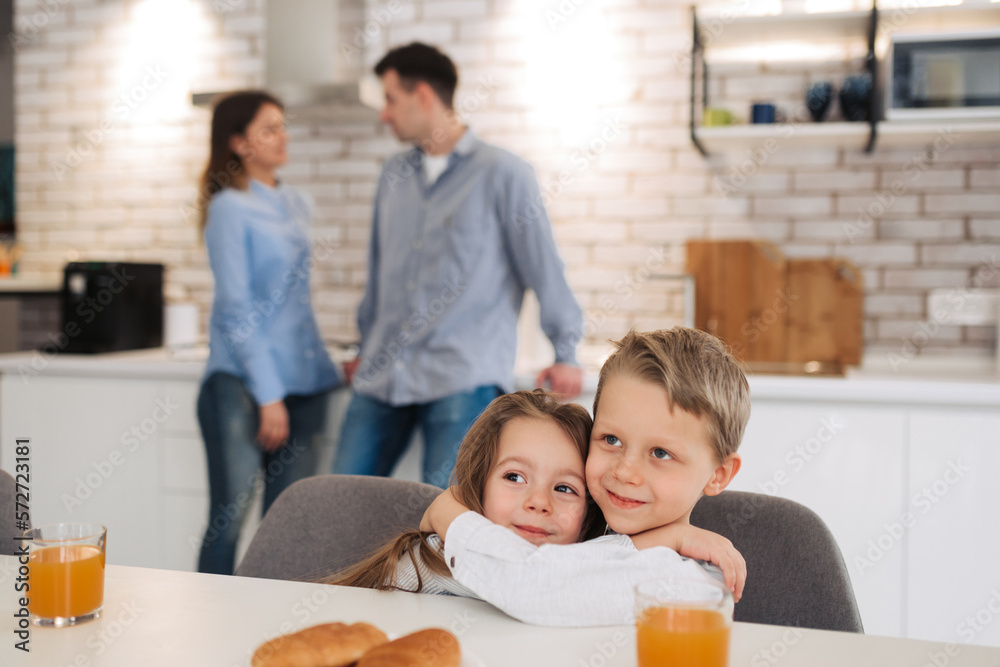 Happy family having breakfast on kitchen. Little girl with brother sitting on kitchen and smiling with their parents on background Happy family having breakfast on kitchen. Little girl with brother sitting on kitchen and smiling with their parents on background