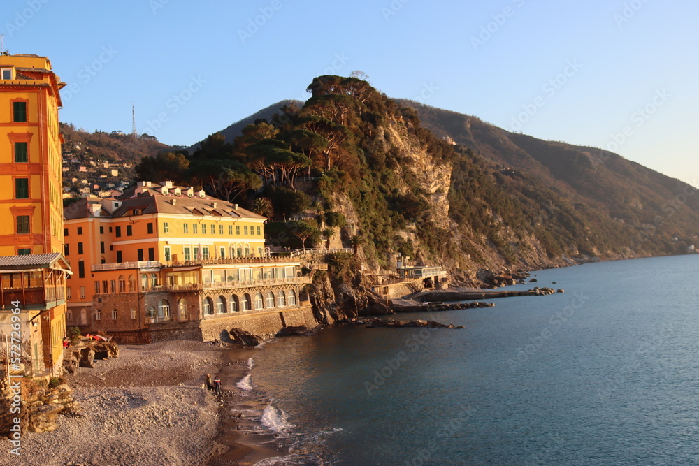 Camogli, Italy - January 27, 2023: Beautiful old mediterranean town at the sunrise time with illumination during winter days. People enjoying the evening at the beach with beautiful sunset background