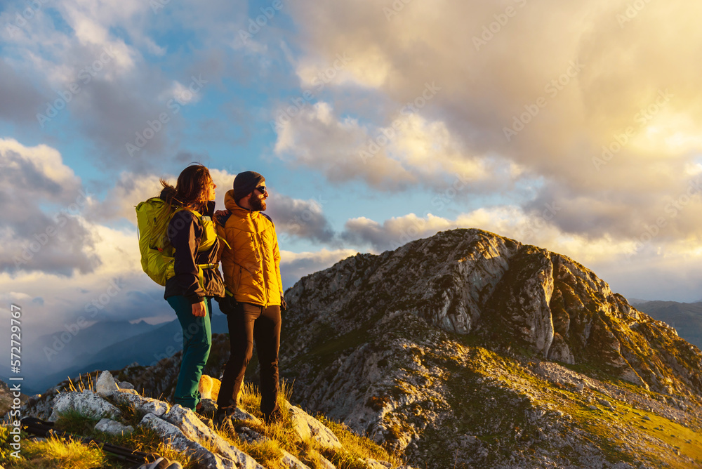 a couple of hikers equipped with mountain equipment, warm clothes and a backpack on top of a mountain watching the sunset. Mountaineers perform exercise in the mountains. sport and outdoor adventure.