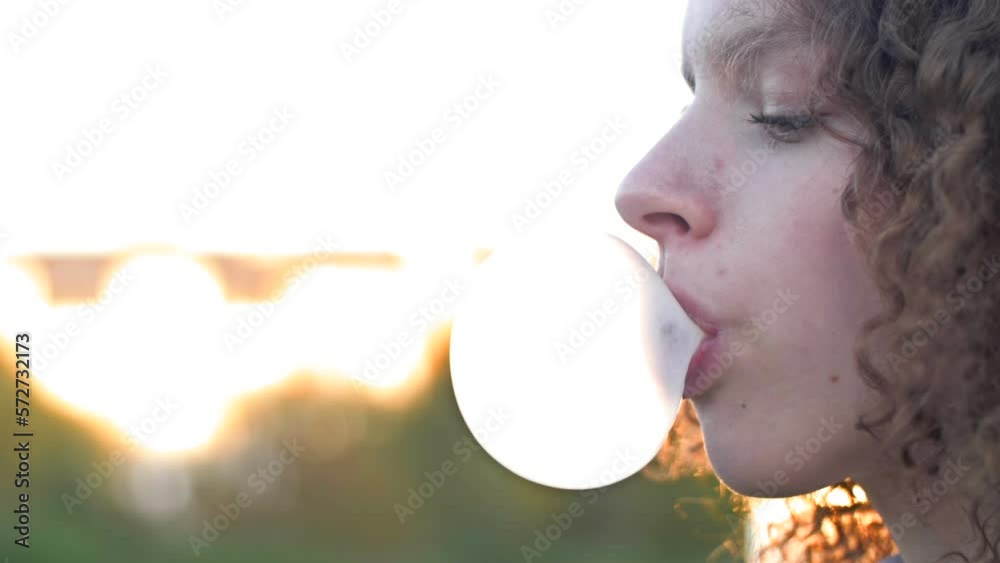 Curly-haired teenage girl inflates a big gum bubble until it bursts.