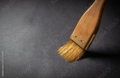 An artistic watercolor brush with a wide wooden handle draws on a black sheet of paper with golden paint. Creative concept. Selective focus, copy space.