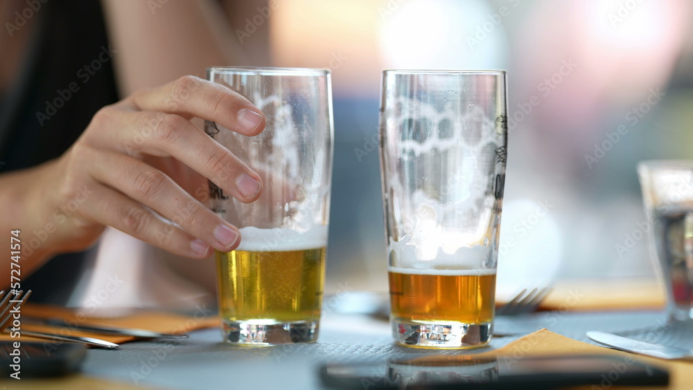 Two half full draft beers at restaurant table. Person hand closeup putting drink down Two half full draft beers at restaurant table. Person hand closeup putting drink down