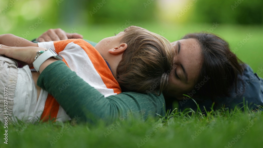 Mother lay on grass with child son. Parenting love and care. Mom laying outdoors with baby toddler Mother lay on grass with child son. Parenting love and care. Mom laying outdoors with baby toddler