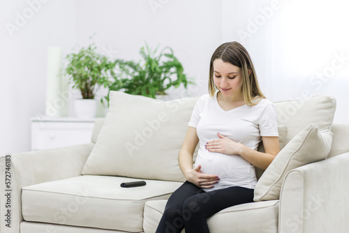 Pregnant woman looking at her belly on white sofa.