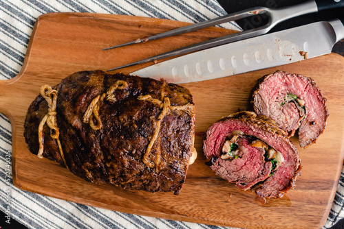 Sliced Stuffed Flank Steak with Prosciutto and Mushrooms on a Cutting Board: Slices of steak roulade stuffed with mushrooms, provolone, and arugula