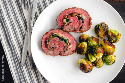 Stuffed Flank Steak with Prosciutto and Mushrooms Dinner: Slices of steak roulade served on a plate with roasted Brussels sprouts photo