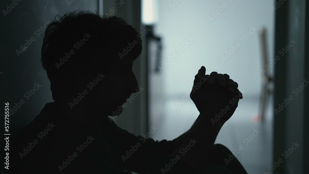 Person covering face in despair sitting on floor in the dark. Dramatic scene of depressed man