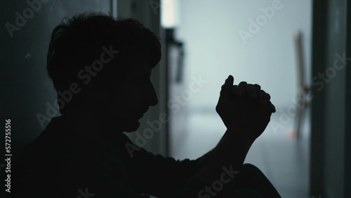 Person covering face in despair sitting on floor in the dark. Dramatic scene of depressed man