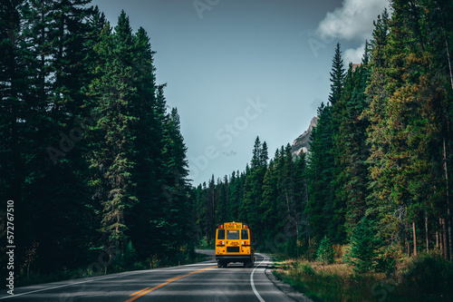 Yellow school bus on a road in the Canadian Rocky Mountains, with green trees and mountains in the background.
