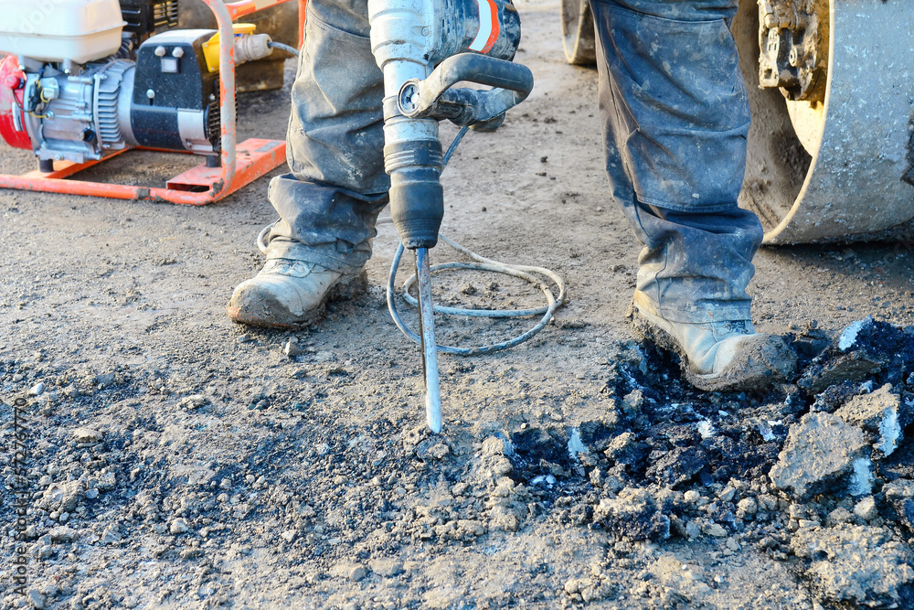 Builder breaking asphalt with electric breaker Builder breaking asphalt with electric breaker