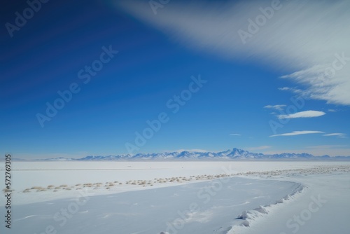 Vast expanse of frozen tundra with snow-covered mountains in the distance and a clear blue sky overhead. Generative AI © Kanisorn