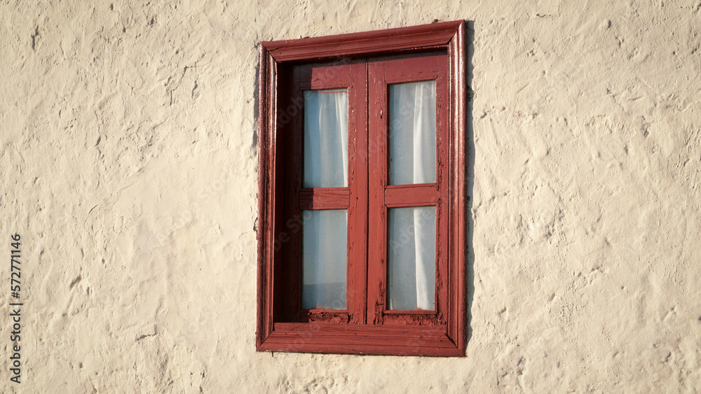 Ventana con marco de madera rojo y cortina en pared de estuco blanco de casa rural