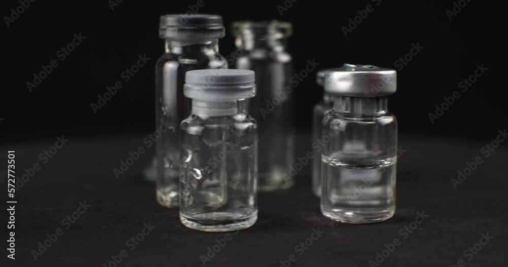 Medicine vials rotate on a black background. The vials are empty and with a transparent medicine stand in a heap on a rotating platform. Glass bottles without labels on a black background. Medicine vials rotate on a black background. The vials are empty and with a transparent medicine stand in a heap on a rotating platform. Glass bottles without labels on a black background.