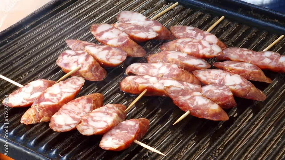 Grilled smoked sausage skewers on sticks - sliced pork meat on hot grill: barbecue. Unhealthy but tasty food containing saturated fats. Grilled smoked sausage skewers on sticks - sliced pork meat on hot grill: barbecue. Unhealthy but tasty food containing saturated fats.