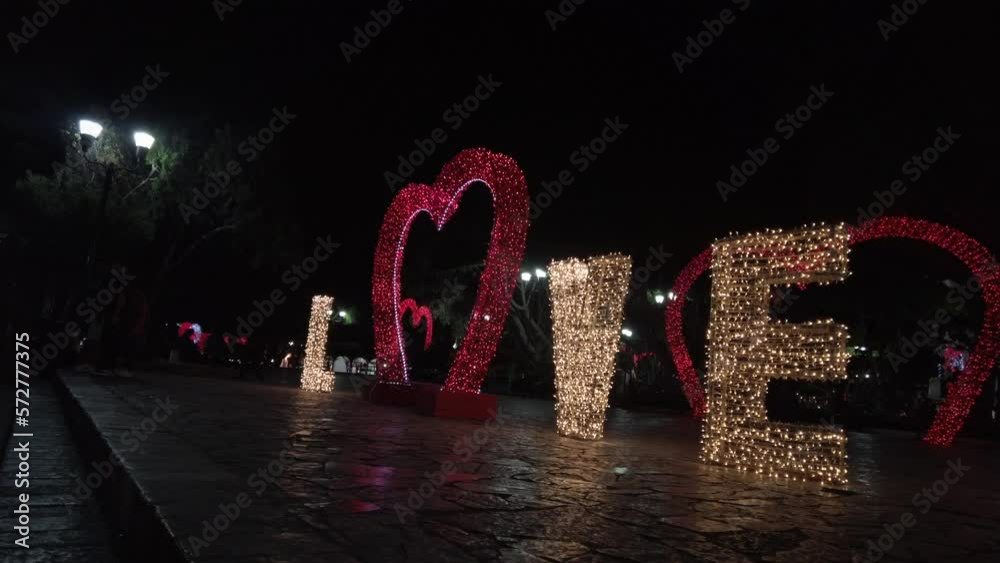 Letrero de amor iluminado con la palabra love escrita, con un corazón rojo iluminado con focos de baja intensidad en la calle 