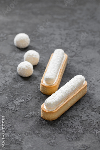 Oval tartlet in the form of eclair "Raffaello" with coconut custard and cream jelly, sprinkled with coconut chips on top. Dark gray background