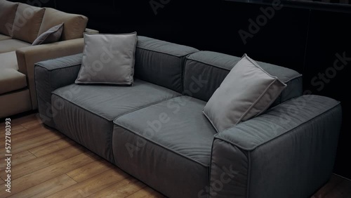 Gray sofa with two pillows filmed in a furniture store, in the background there is a comfortable brown sofa. 4k video.