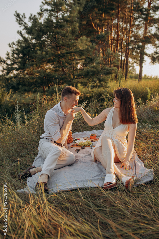 A guy kisses his girlfriend's hand while sitting on a picnic in the forest. Lovestory at sunset in summer. Warm family shooting in nature A guy kisses his girlfriend's hand while sitting on a picnic in the forest. Lovestory at sunset in summer. Warm family shooting in nature