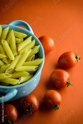 Top view of cherry tomatoes and raw pasta in bowl on red surface