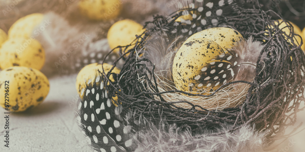 Holiday still life with decorative quail eggs in a brown nest among feathers. Easter decor with selective focus