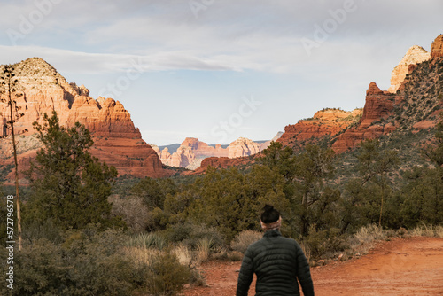 Woman hiker standing on Bell Rock trail in red rock formations within coconino national forest in Sedona Arizona USA against white cloud background.