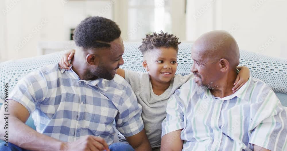 Smiling african american son between happy father and grandfather on couch at home, slow motion Smiling african american son between happy father and grandfather on couch at home, slow motion
