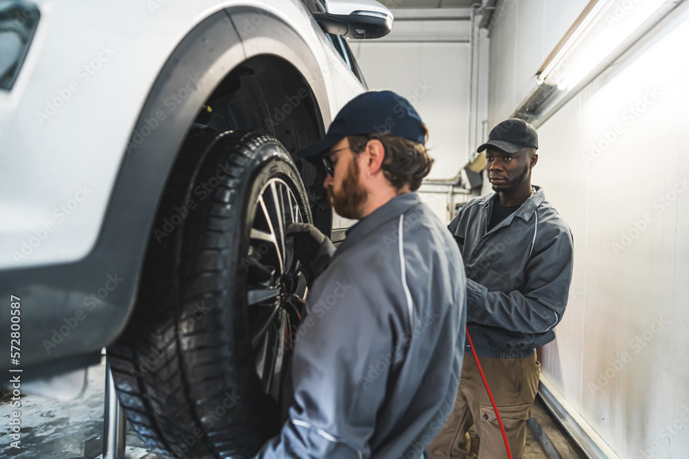 Two mechanics at work. One changing a tyre, another looking at thr first one. High quality photo Two mechanics at work. One changing a tyre, another looking at thr first one. High quality photo