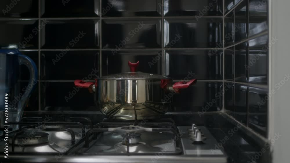 hand of man in gray sweater put pot of food on gas stove to heat soup. lonely man heats up his own food for lunch. Preparation for cooking on gas burner. hand of man in gray sweater put pot of food on gas stove to heat soup. lonely man heats up his own food for lunch. Preparation for cooking on gas burner.