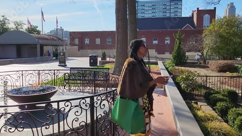 An African American woman with long sisterlocks standing in The King Center using a mobile phone wearing a brown fur carrying a green purse surrounded by lush green trees and plants in Atlanta Georgia photo