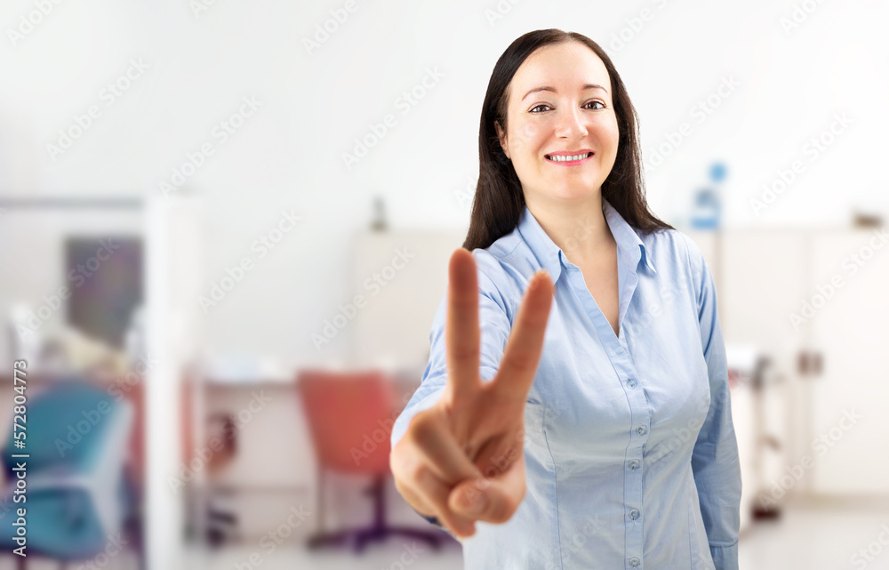Portrait of a confident young businesswoman showing a victory gesture in a modern office