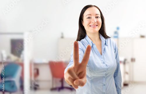 Portrait of a confident young businesswoman showing a victory gesture in a modern office © cunaplus