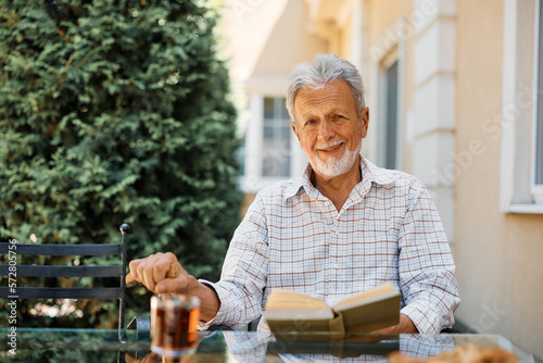 Smiling elderly man reads book on patio at independent living community.