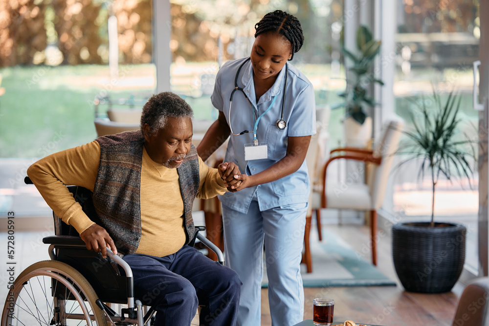 Young black nurse assists senor man to get up from wheelchair at nursing  home. Stock Photo | Adobe Stock