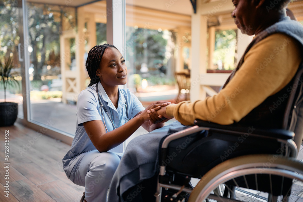 Caring black nurse comforting senior man in wheelchair at nursing home