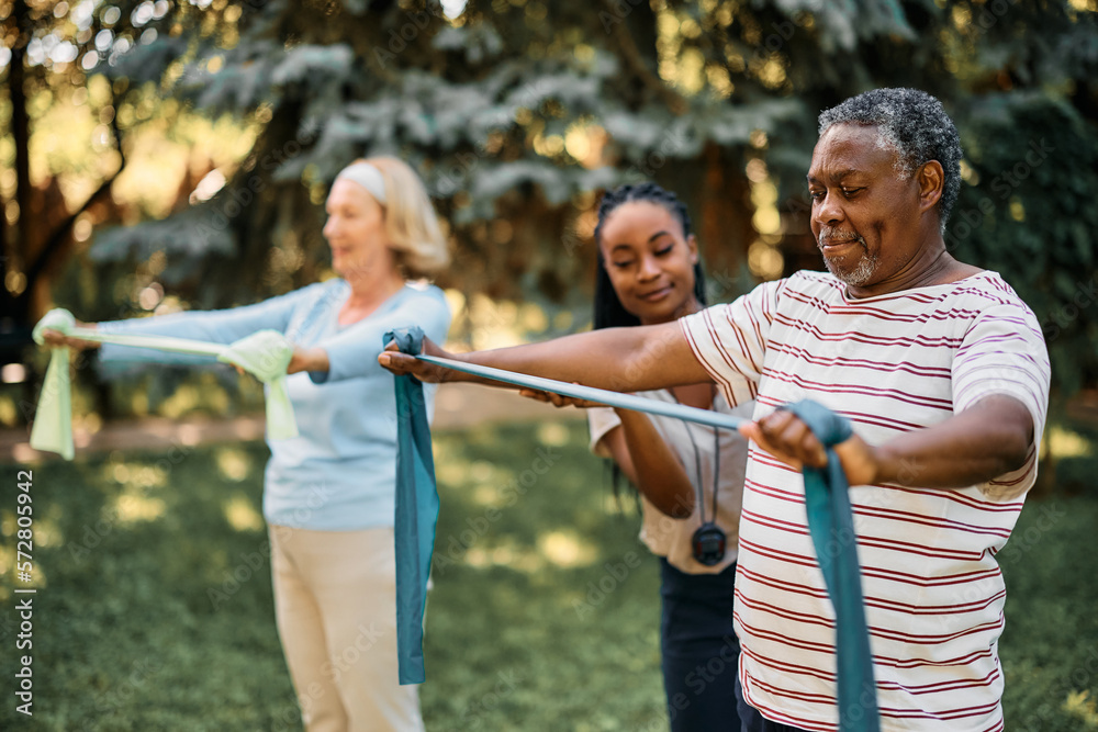 © Drazen - Black senior man practicing with power band on exercise class at residential care home.