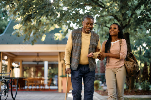 Happy black woman walks with her senior father while visiting him at nursing home. photo