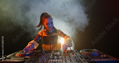 Cool female asian dj is working in a nightclub, standing at turntables, creating a dance music set - nightlife concept 