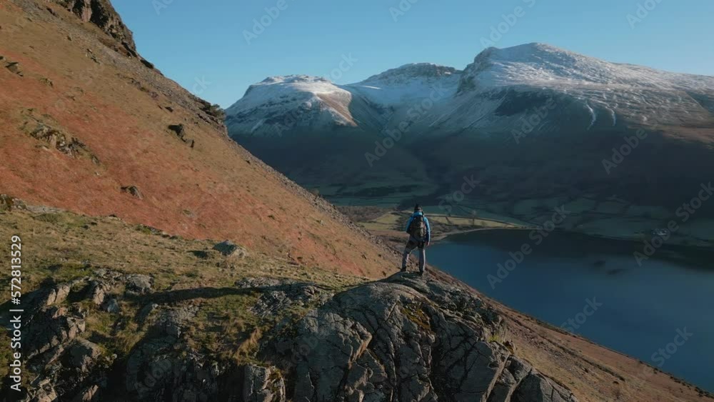 Hiker on mountain with reveal of snowy mountains and dark lake with bright sun and natural lens flare at Wasdale Lake District UK Hiker on mountain with reveal of snowy mountains and dark lake with bright sun and natural lens flare at Wasdale Lake District UK