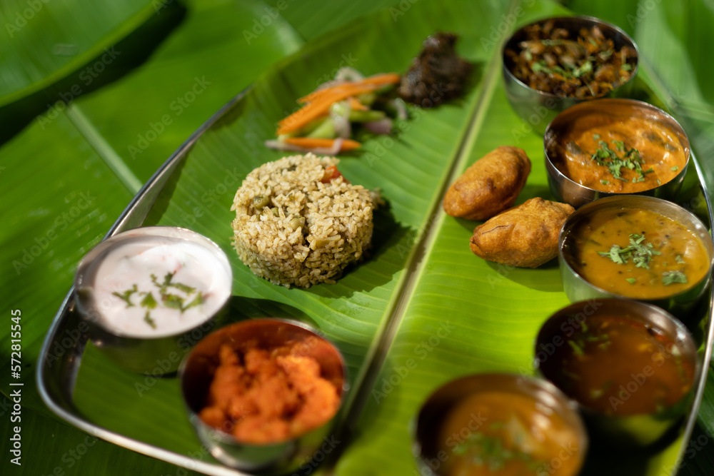 Beautifully served on banana leaves as a traditional meal plate in south India, a variety of small dishes are served including yogurt, sauces, chutneys, rice, and dumplings.