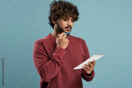 Canvas-taulu Confident thoughtful young Hindu man writing the list to do on notepad over isol