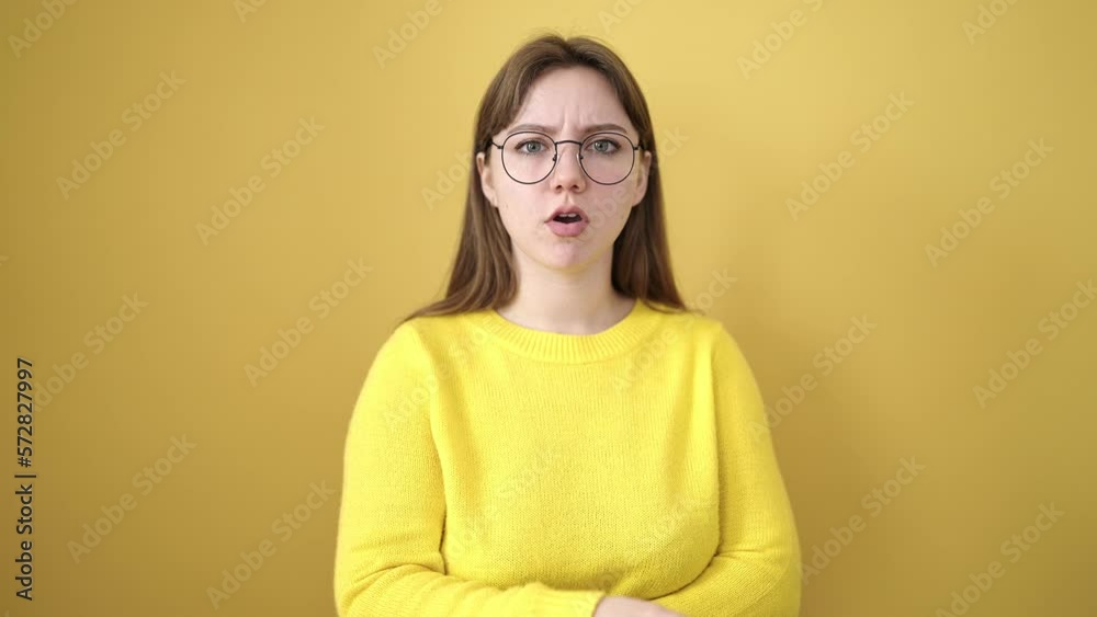 Young blonde woman standing with arms crossed gesture over isolated yellow background Young blonde woman standing with arms crossed gesture over isolated yellow background