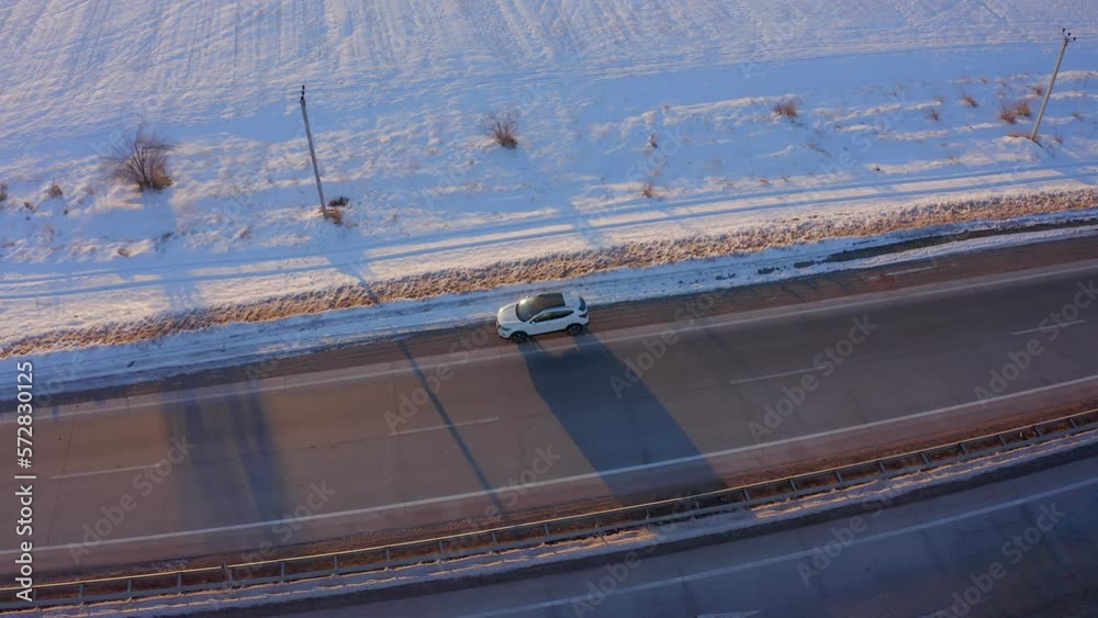 Aerial view, a white car stands by the side of the road in the steppe covered with snow. A truck drives past a car parked on the side of the road Aerial view, a white car stands by the side of the road in the steppe covered with snow. A truck drives past a car parked on the side of the road