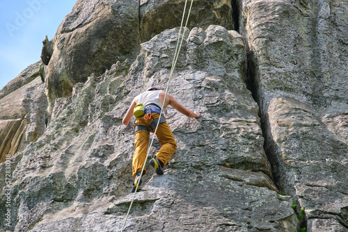 Determined climber clambering up steep wall of rocky mountain. Sportsman overcoming difficult route. Engaging in extreme sports and rock climbing hobby concept